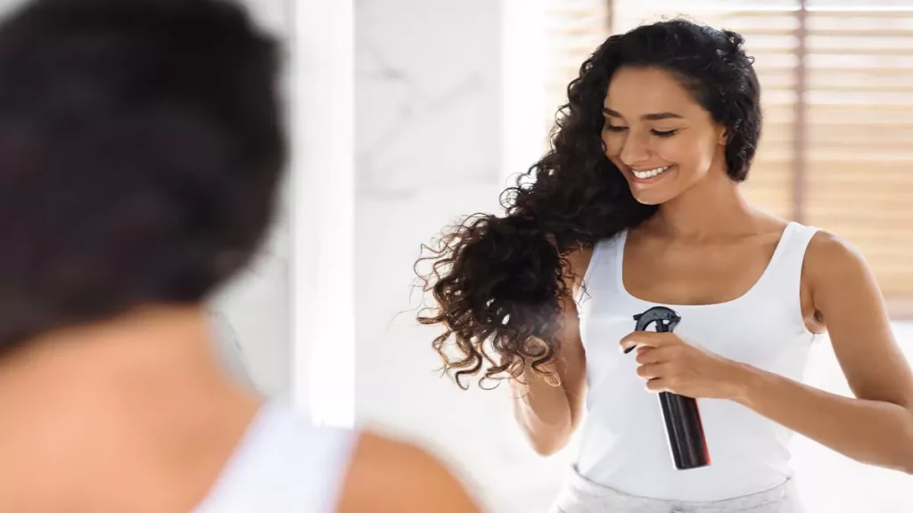 Mulher com cabelo cacheado aplicando spray de protetor térmico