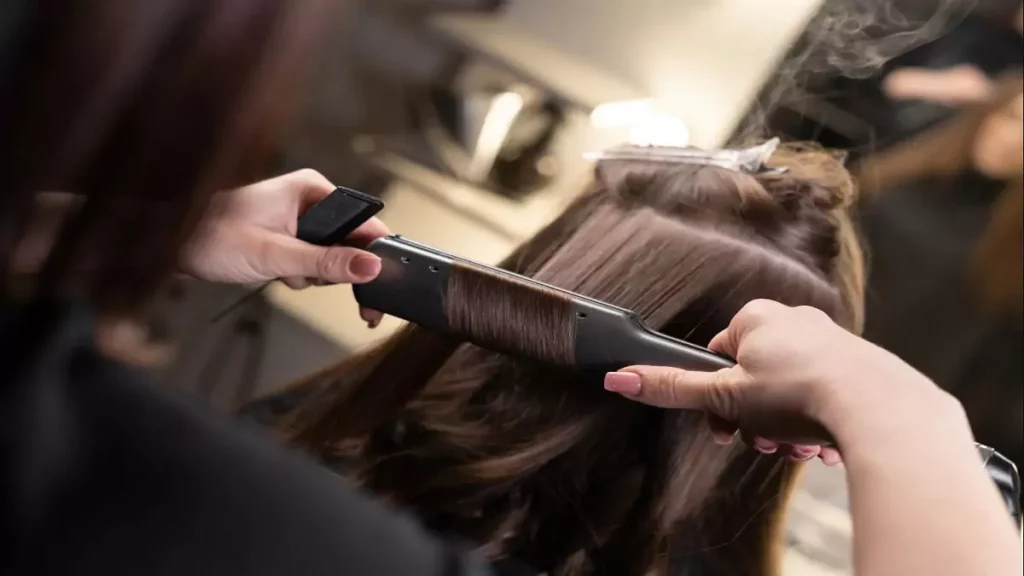 Cabelereira usando uma chapinha para progressiva no cabelo de cliente