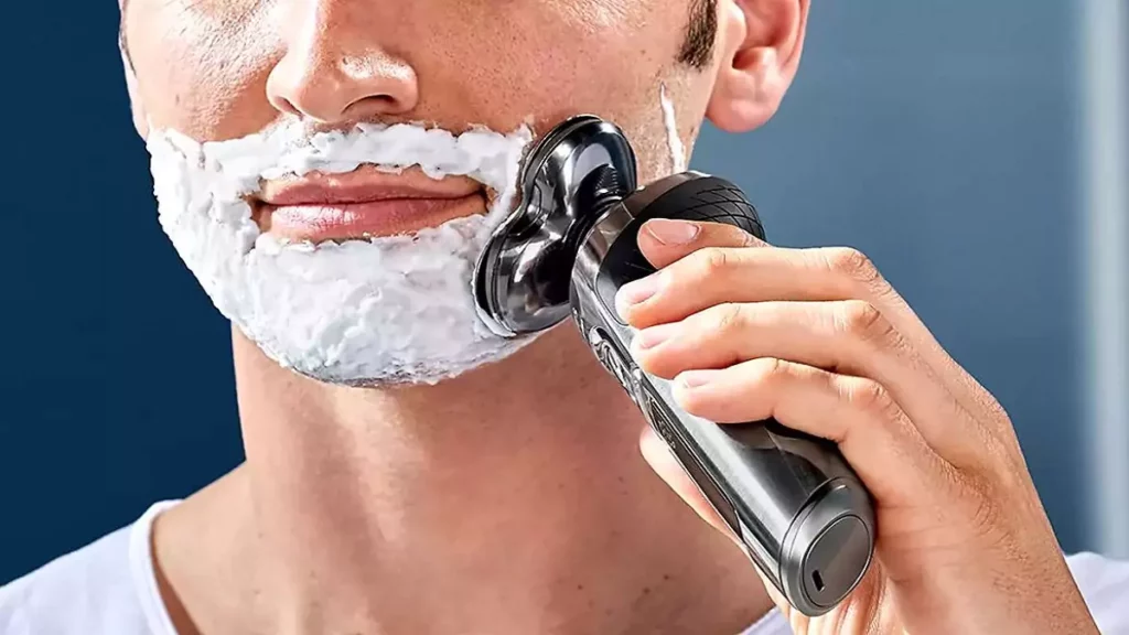 Homem fazendo a barba com espuma e barbeador elétrico